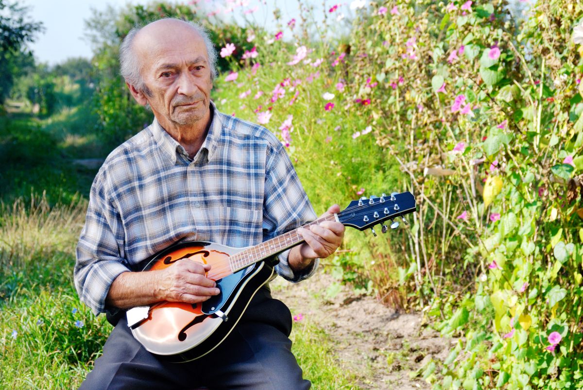 A senior man playing the mandolin outside in his garden